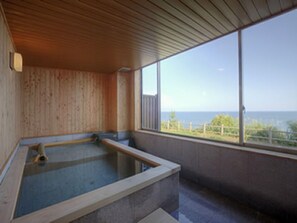 Un cuarto de spa con techo de madera, una bañera de piedra y vista al mar.
