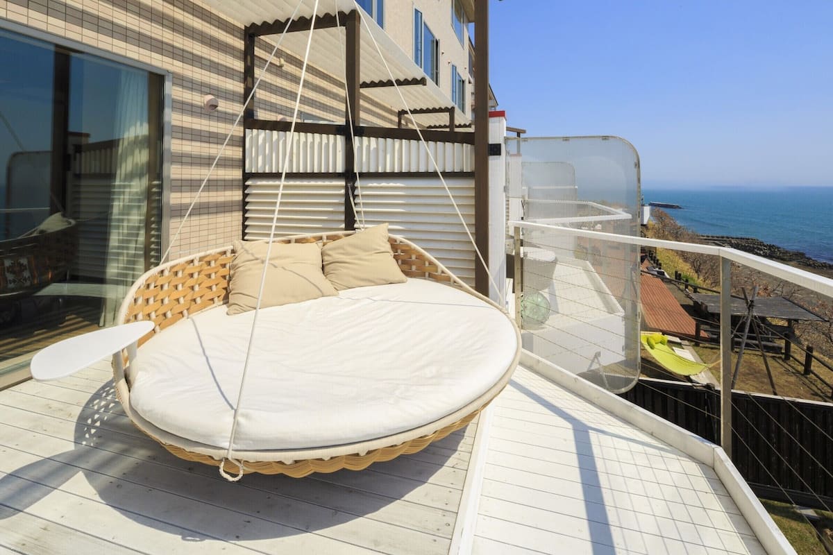 Un balcón con una silla colgante, una mesita y vista al mar.