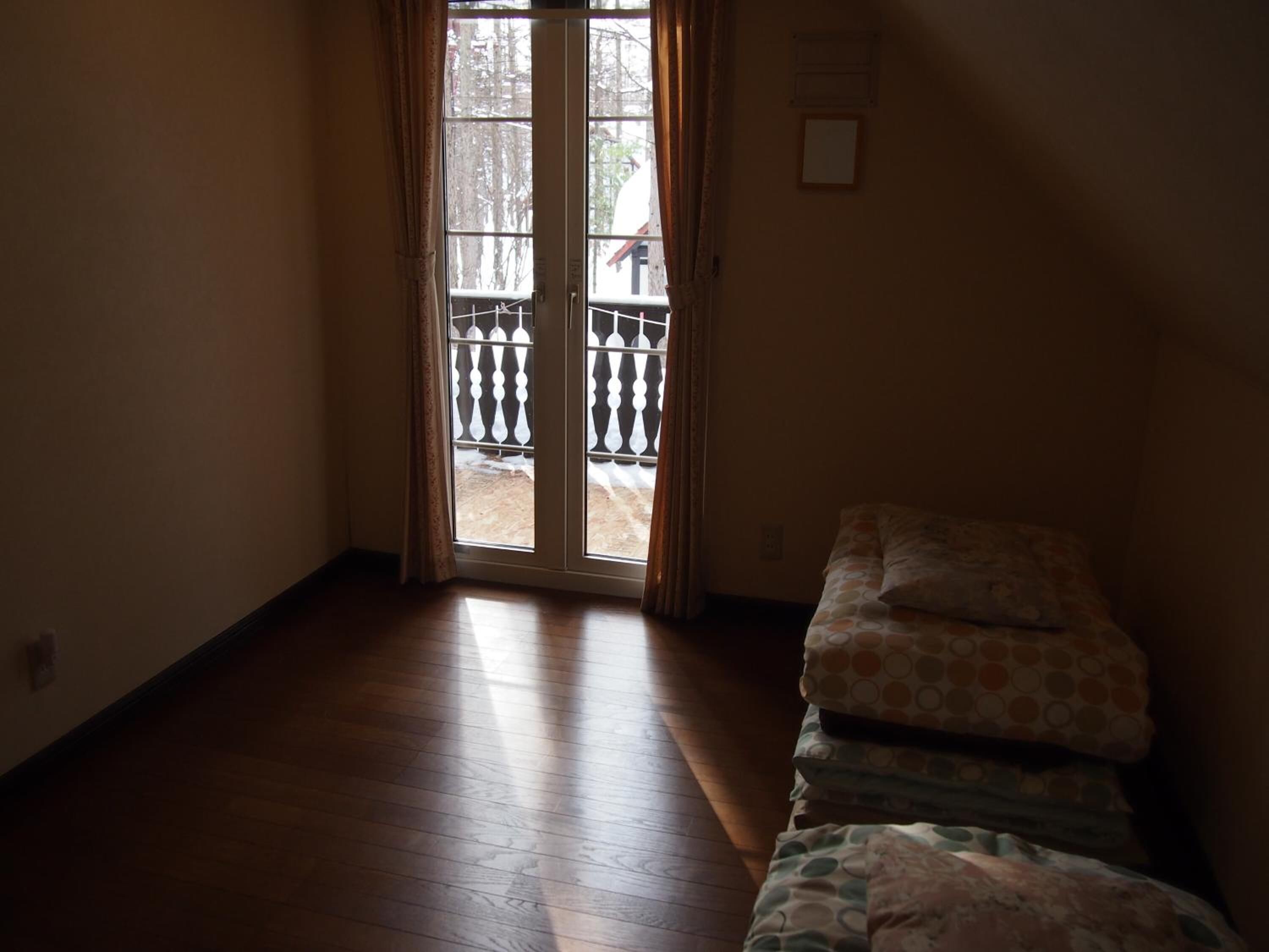 A room with a wooden floor, a bed with patterned bedding, and a sliding glass door leading to an outdoor area with a railing.