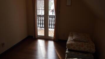A room with a wooden floor, a bed with patterned bedding, and a sliding glass door leading to an outdoor area with a railing.