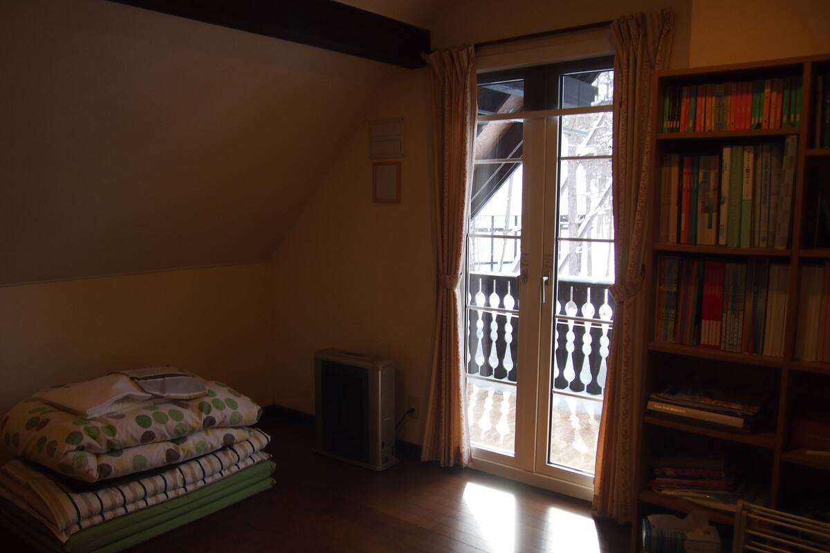 A room with a bed, a radiator, a bookshelf, and a window with curtains.