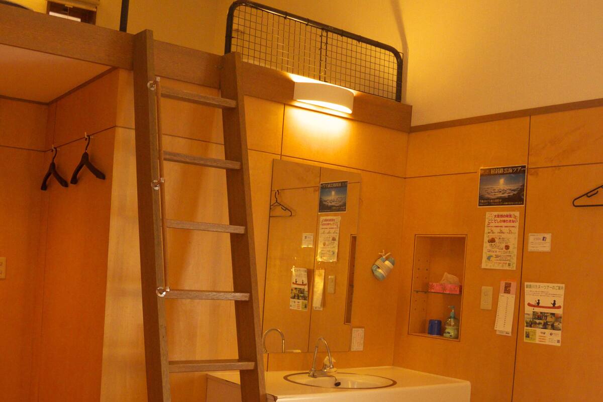 A bedroom with a bunk bed, a wooden ladder, a sink, and a mirror.
