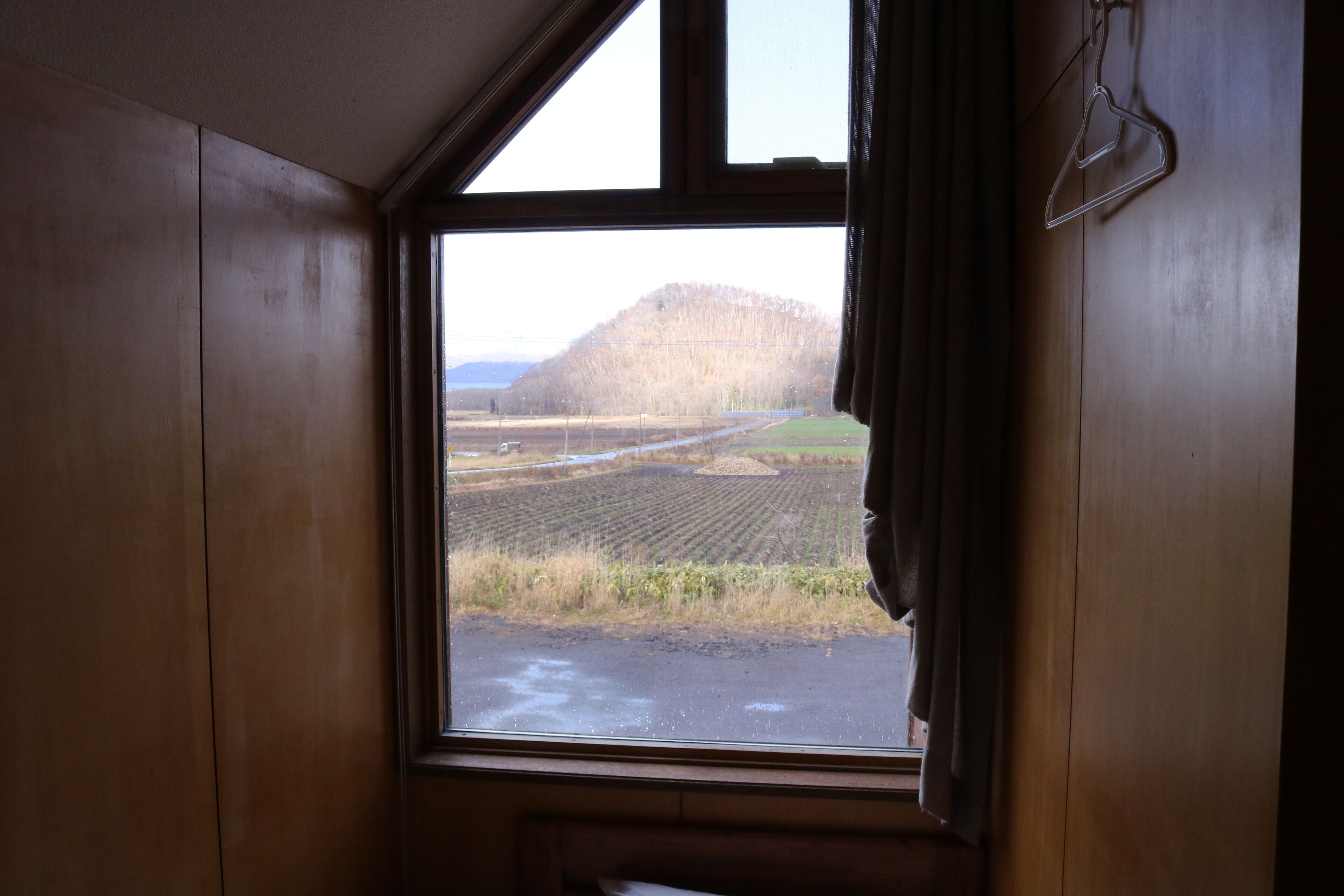 A window with a view of a field and a hill.