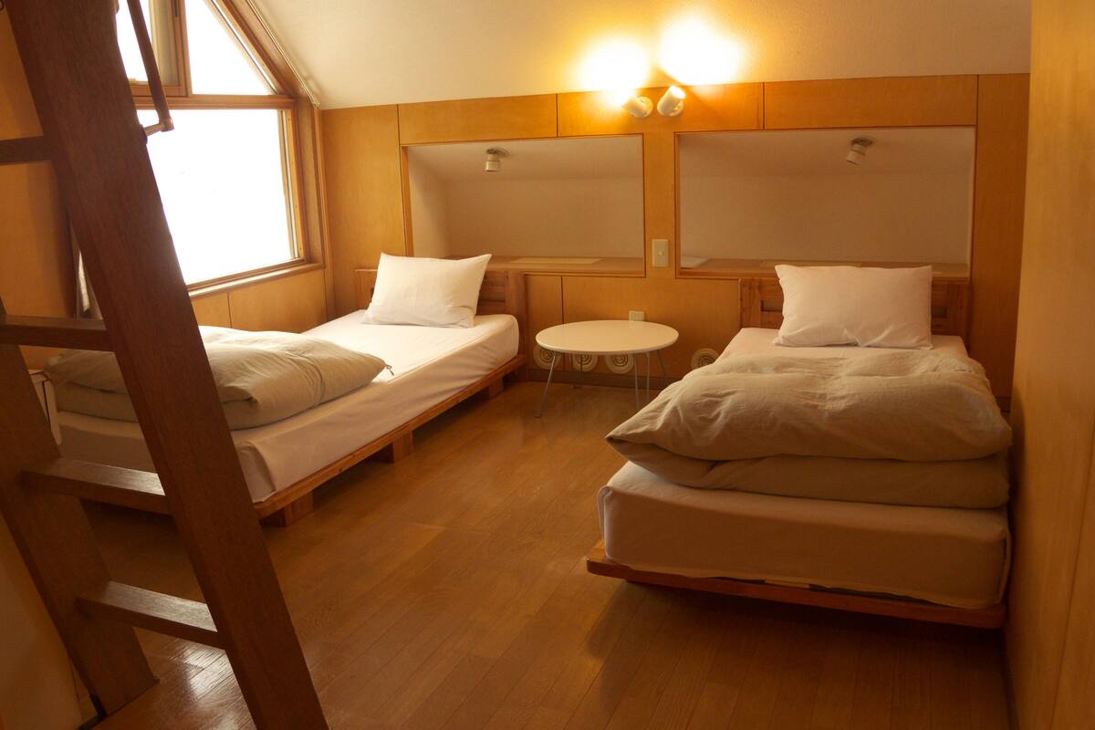 A room with two single beds, a small round table, and a window with natural light.
