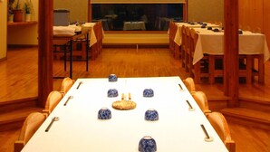 A dining area with a long table, multiple chairs, and a high ceiling with a skylight. - Kussharo Genya Youth Guesthouse – Hostel (Teshikaga)