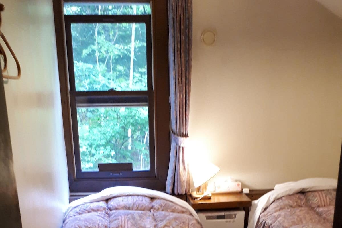 Quarto com duas camas, janela com cortinas, aquecedor e porta.