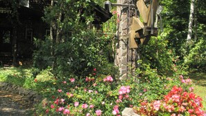 A stone signpost with a directional arrow, surrounded by lush greenery and pink flowers. - Pension & Restaurant Bistare Kana (Niseko)