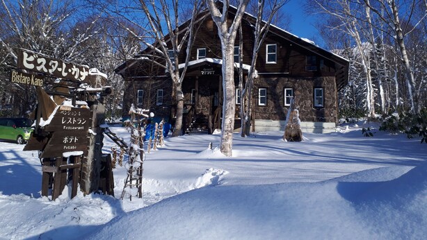 A rustic wooden building with a stone facade, surrounded by snow-covered trees. - Pension & Restaurant Bistare Kana (Niseko)