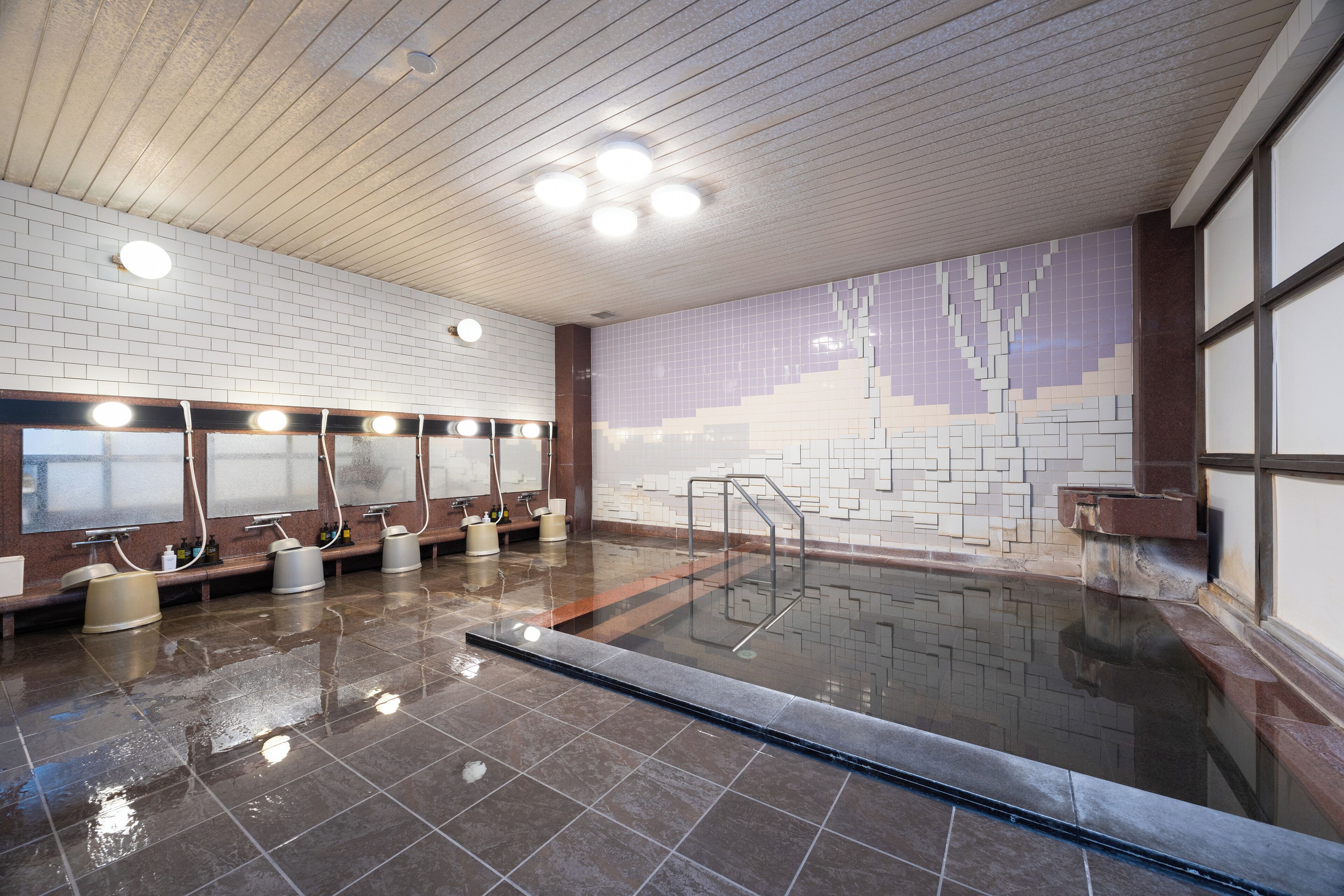 A swimming pool with a tiled wall, benches, and lights.