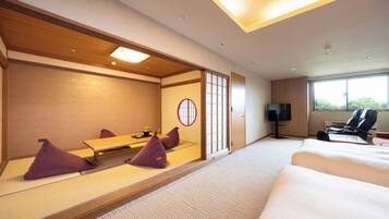 A hotel room with tatami flooring, a traditional Japanese room divider, a bed, a desk with a chair, and a television.