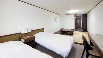 A hotel room with two beds, a desk, a chair, a small table, and a door leading to another room.