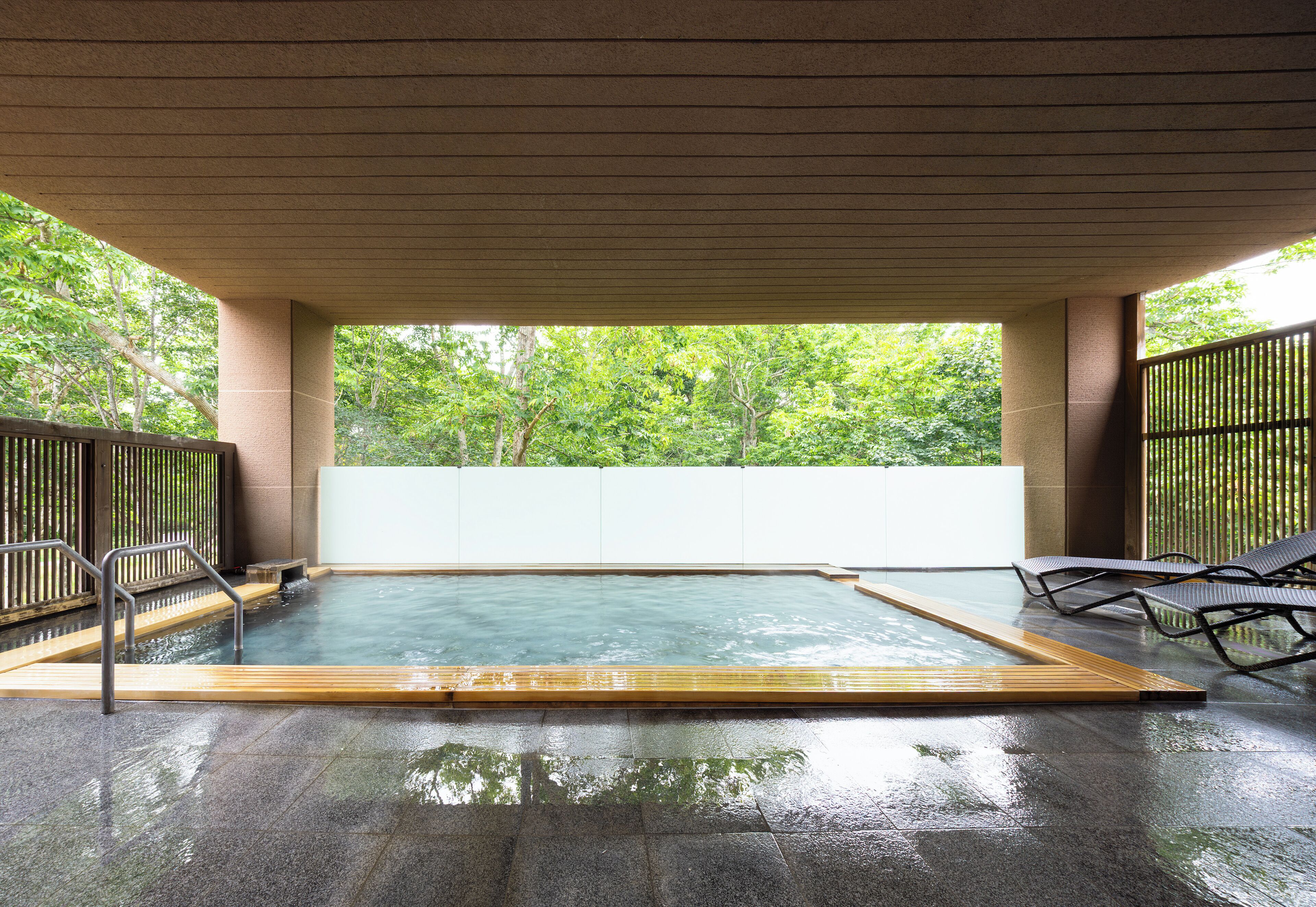 An indoor swimming pool with a wooden deck, metal railings, and lounge chairs.