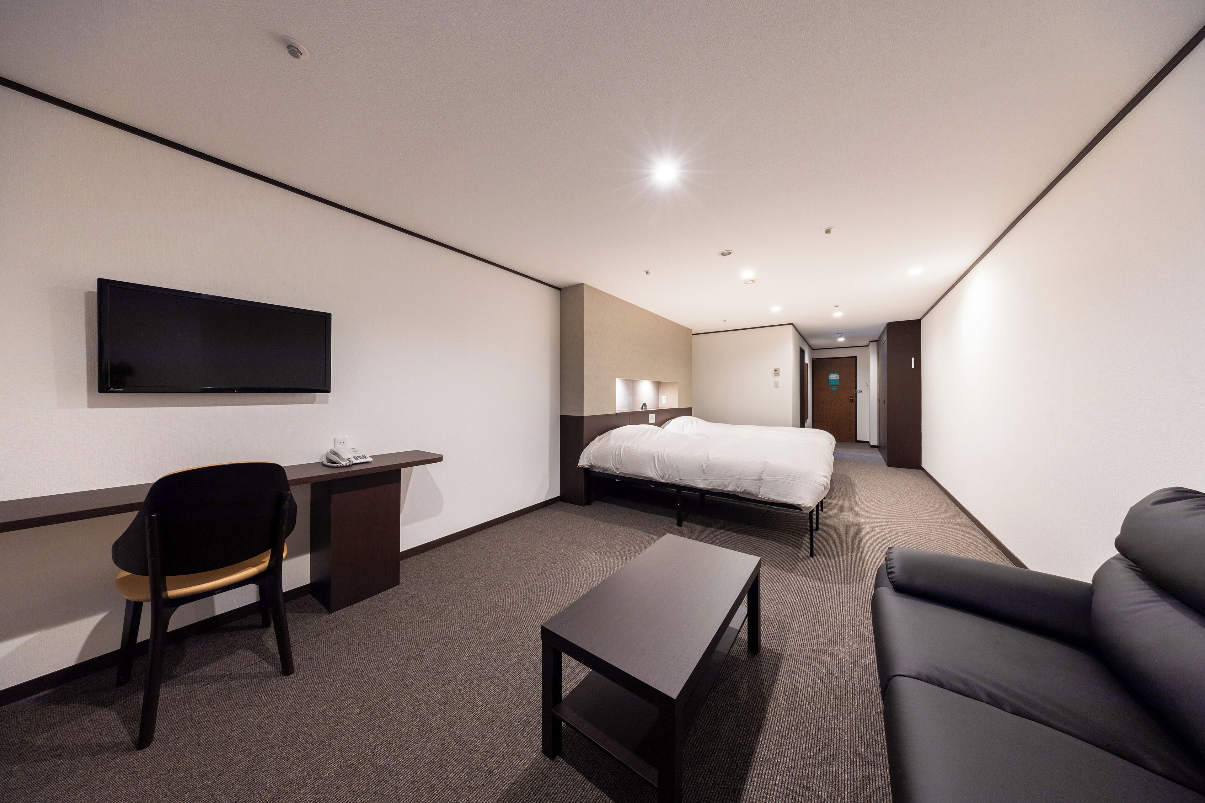 A hotel room with a bed, a desk, a chair, a TV, and a sofa.