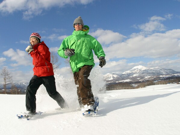 Dos personas caminando con raquetas de nieve sobre un paisaje nevado con montañas al fondo.