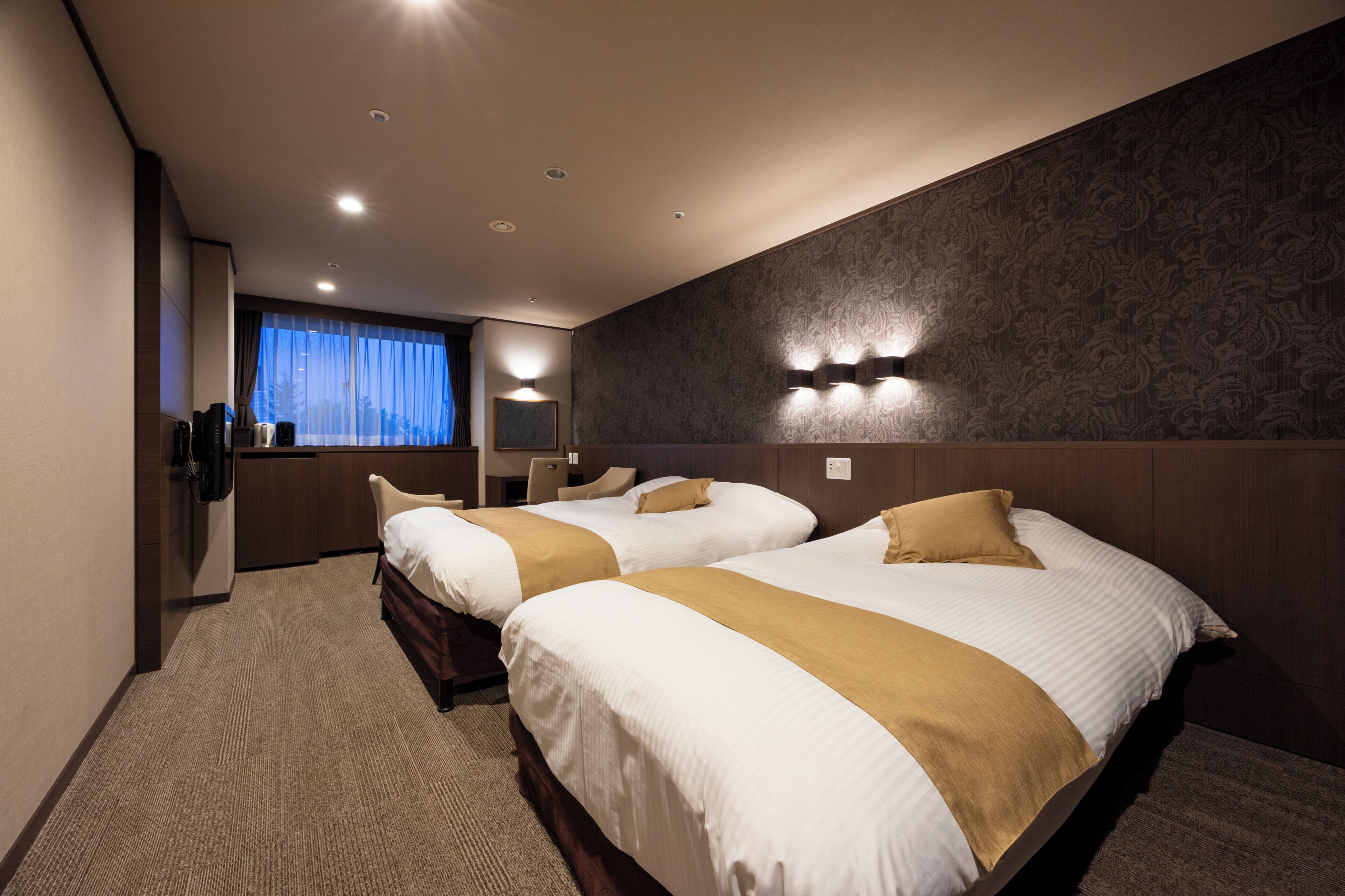 Habitación de hotel con dos camas, un ventanal con cortinas, un espejo en la pared y piso alfombrado.