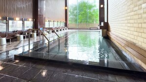 Una amplia piscina interior con múltiples duchas y vistas a árboles a través de grandes ventanales.