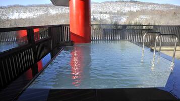 A hot tub with a wooden deck and metal railings, surrounded by a red column and a view of a snowy landscape.