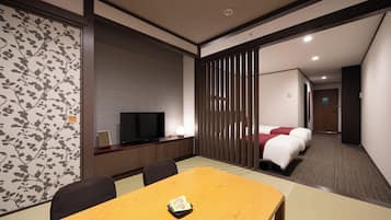 A hotel room with a wooden dining table, a TV, a bed, and a sliding door.