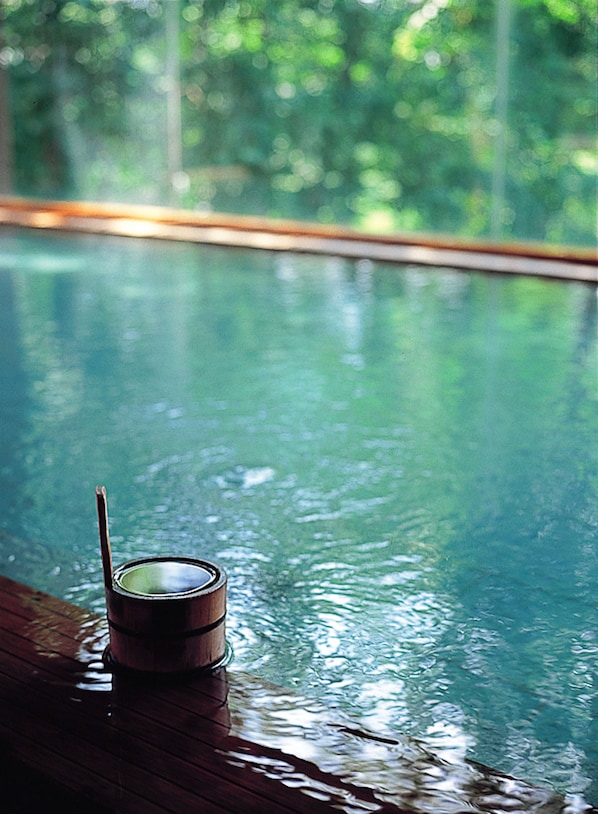 Une terrasse en bois avec un petit bain en bois et une cuillère, donnant sur une piscine aux eaux claires et offrant une vue sur les arbres.