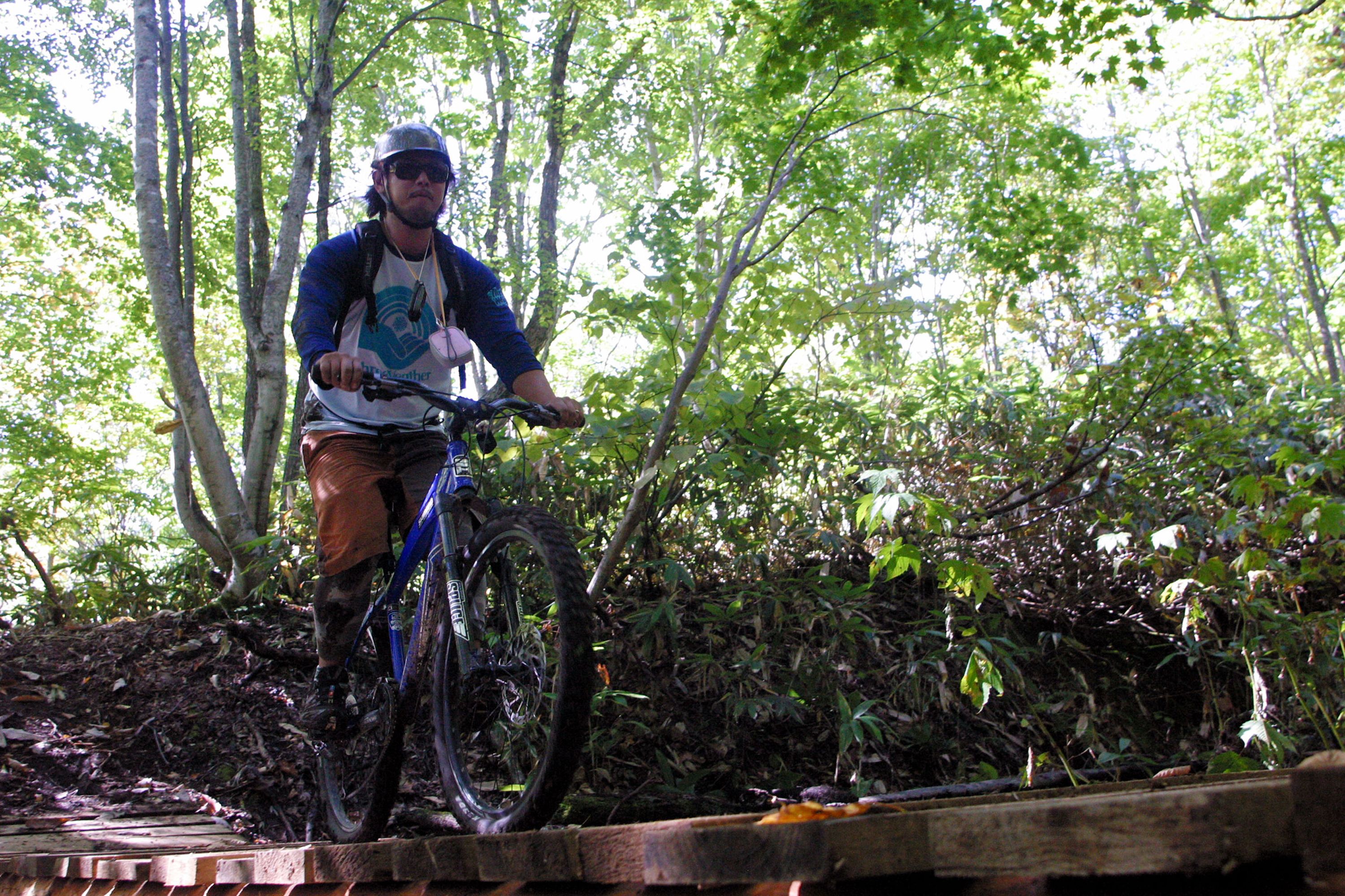 A person riding a mountain bike on a wooden bridge in a forested area.