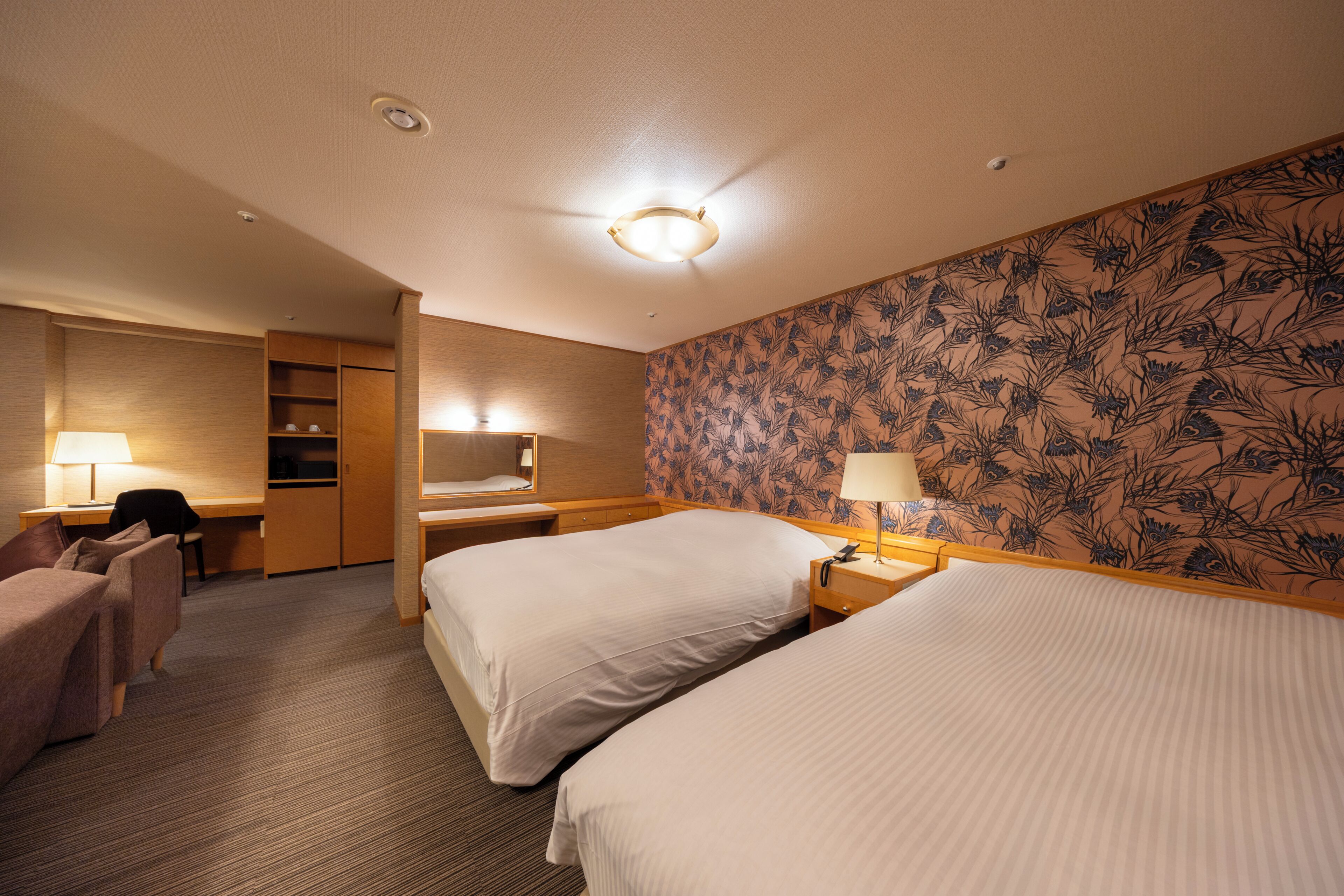 A hotel room with two beds, a desk, a chair, a wardrobe, and a bathroom.