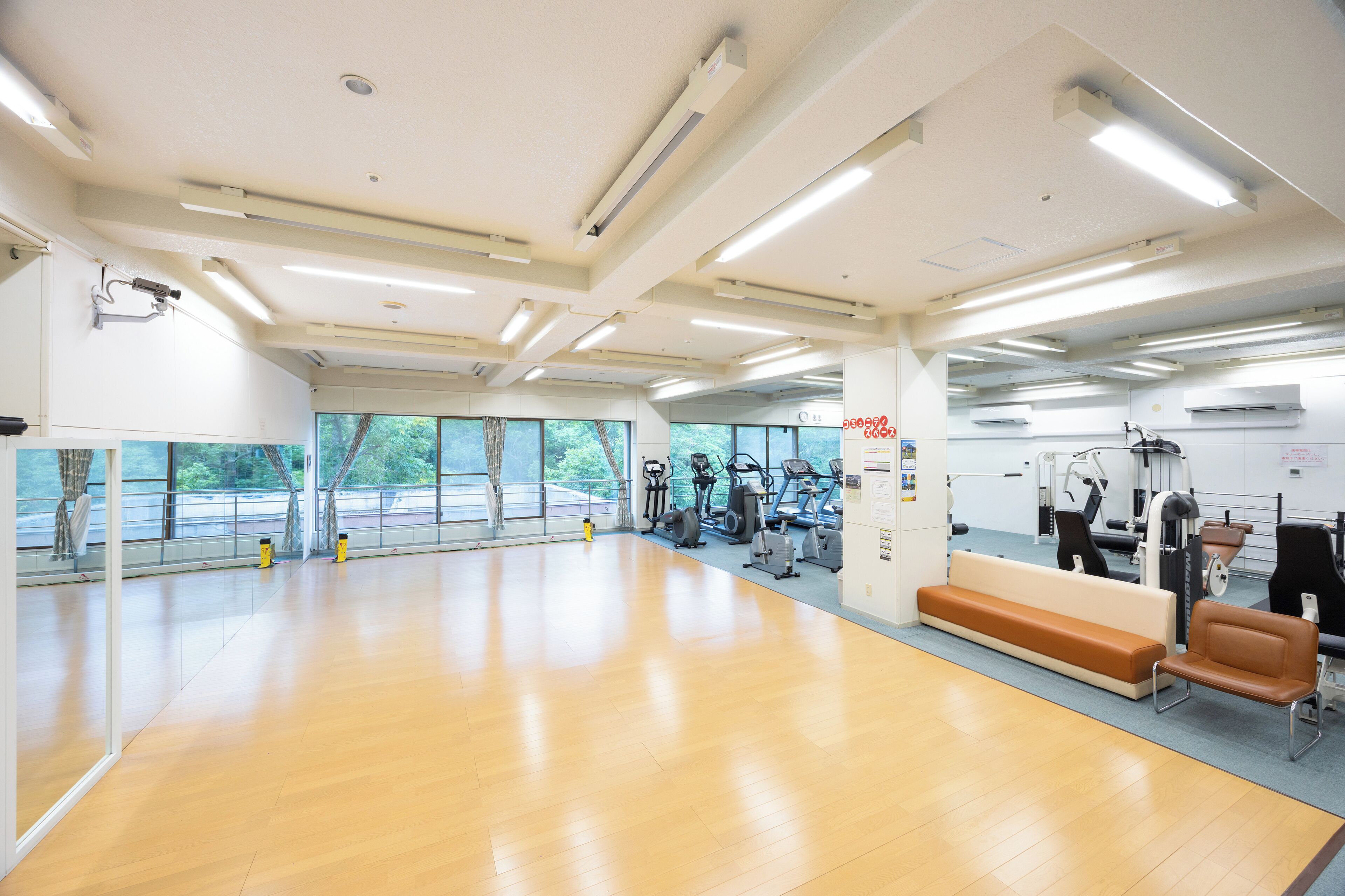 A spacious gym with exercise equipment, large windows, and a wooden floor.
