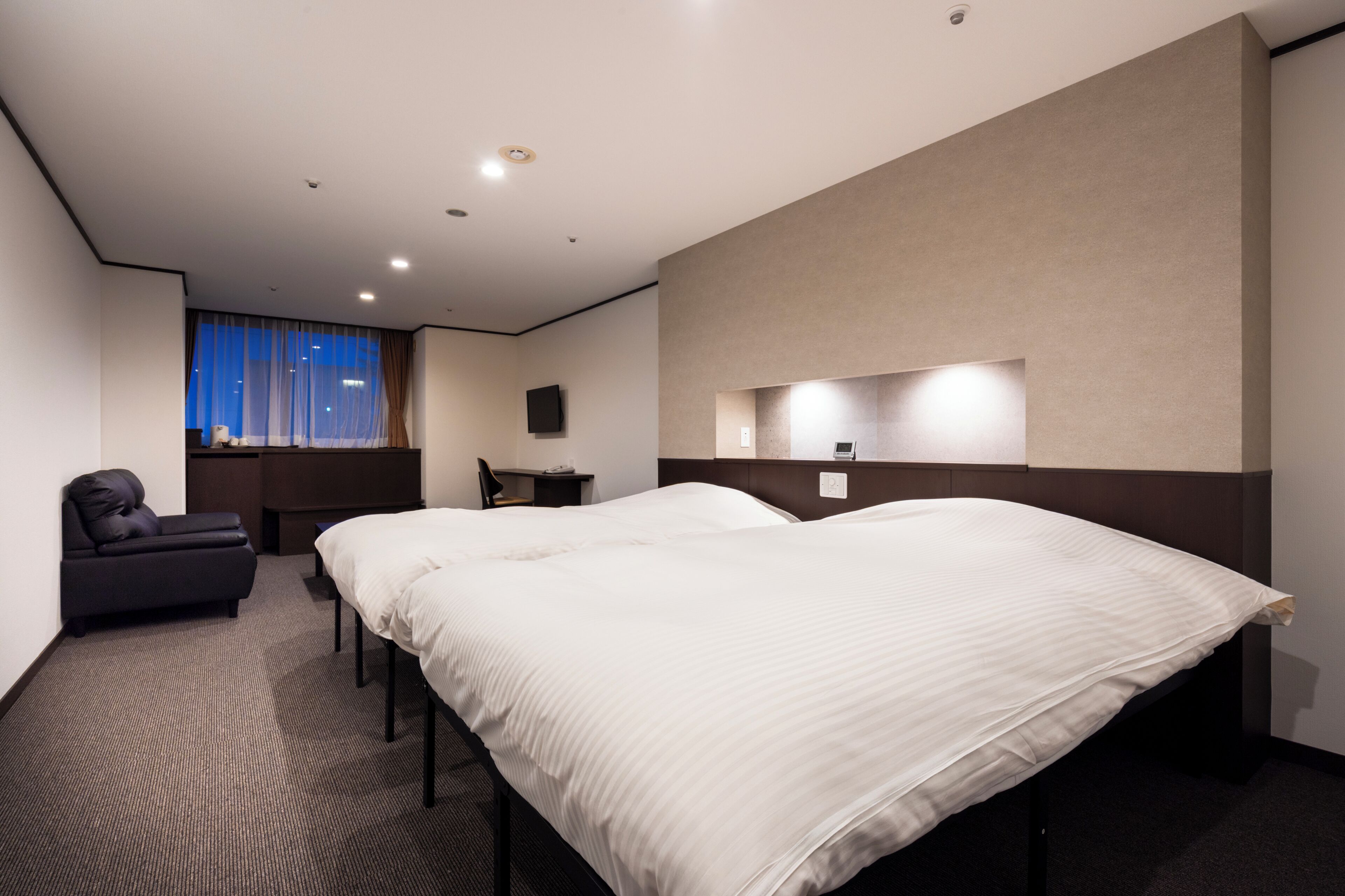A hotel room with a large bed, a desk, a chair, a TV, and a window with curtains.