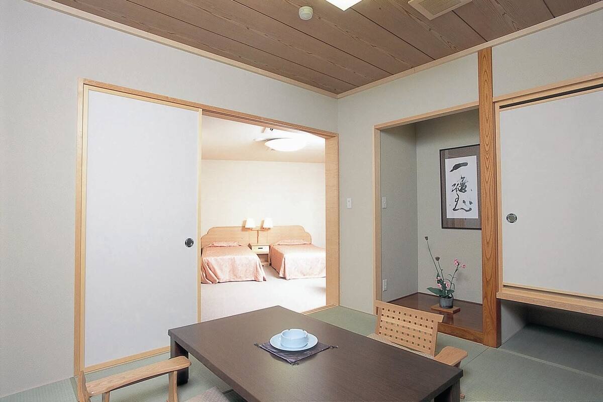 A traditional Japanese room with tatami flooring, a low wooden table, and a bed with pink bedding.