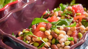 Close-up van een kleurrijke salade met verschillende bonen, tomaten en groene bladgroenten in een glazen schaal.