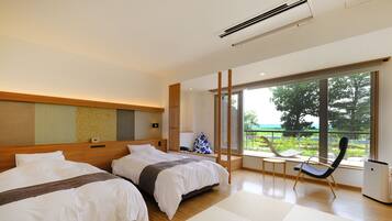 A modern hotel room with two beds, a small table, a chair, and a large window offering a view of greenery.