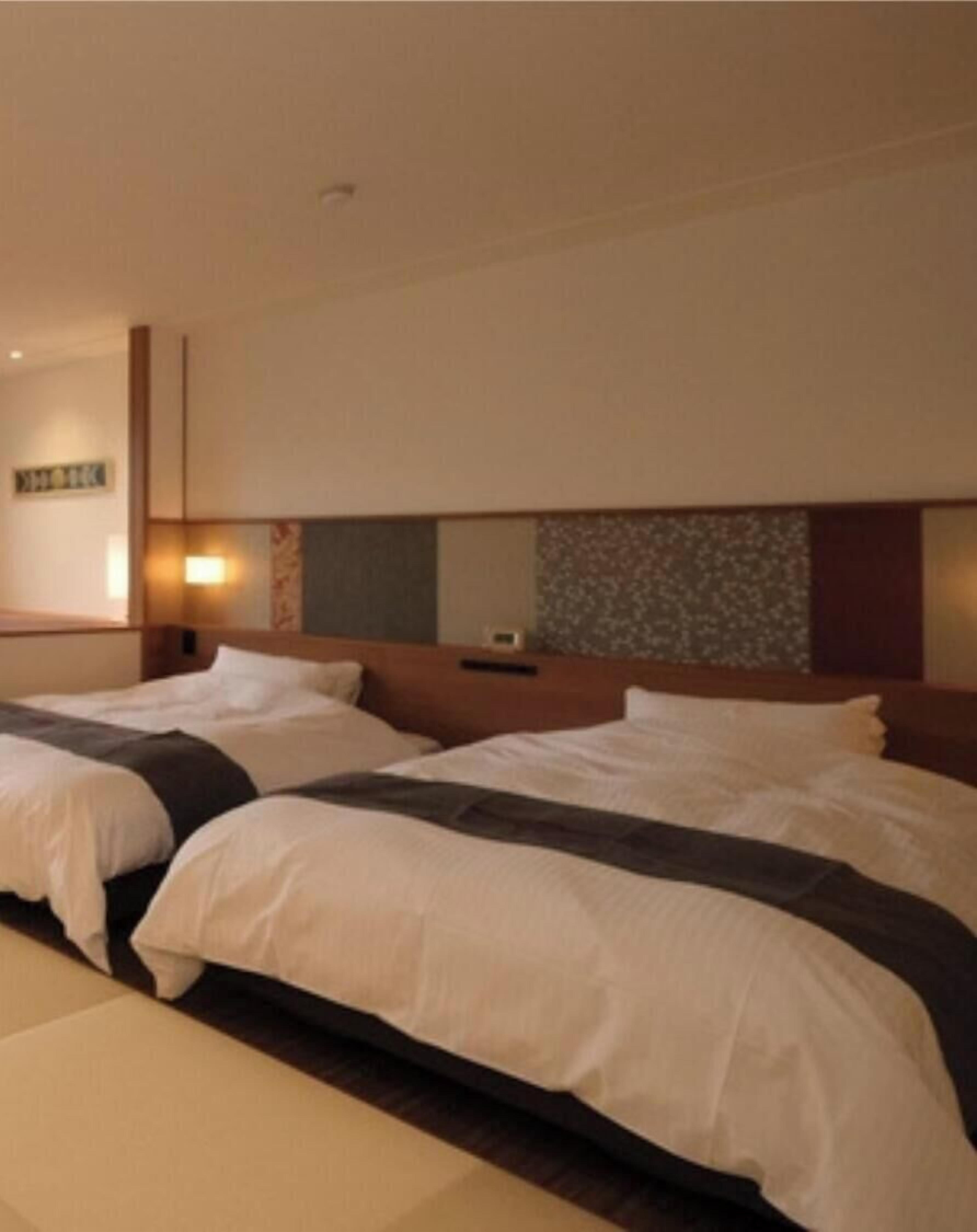 Ein Hotelzimmer mit zwei Betten, einem Kopfteil mit Spiegel und einer Wandleuchte.