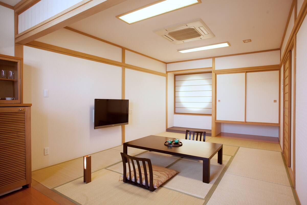 A traditional Japanese-style room with tatami flooring, a low table, chairs, a television, and sliding doors.