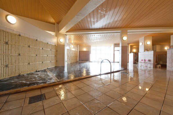 A spacious indoor swimming pool with a bamboo wall, tiled floor, and multiple ceiling lights.