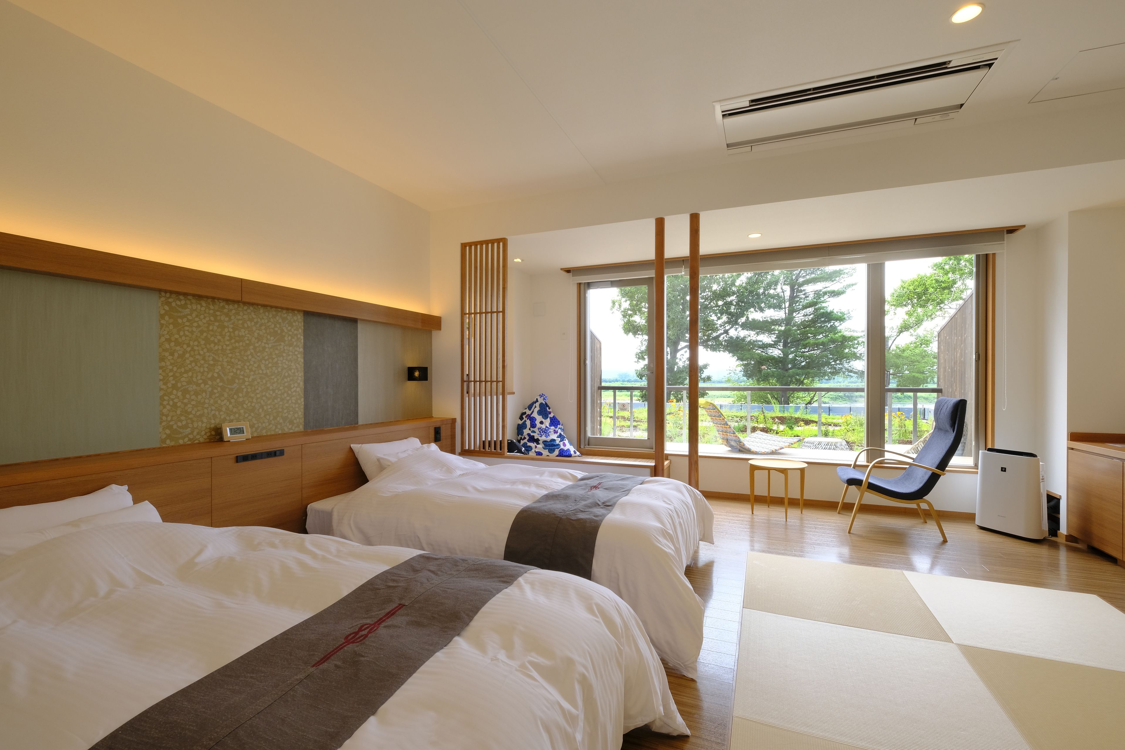 Habitación de hotel con dos camas, vistas al exterior y un área de descanso con una silla y una mesa.