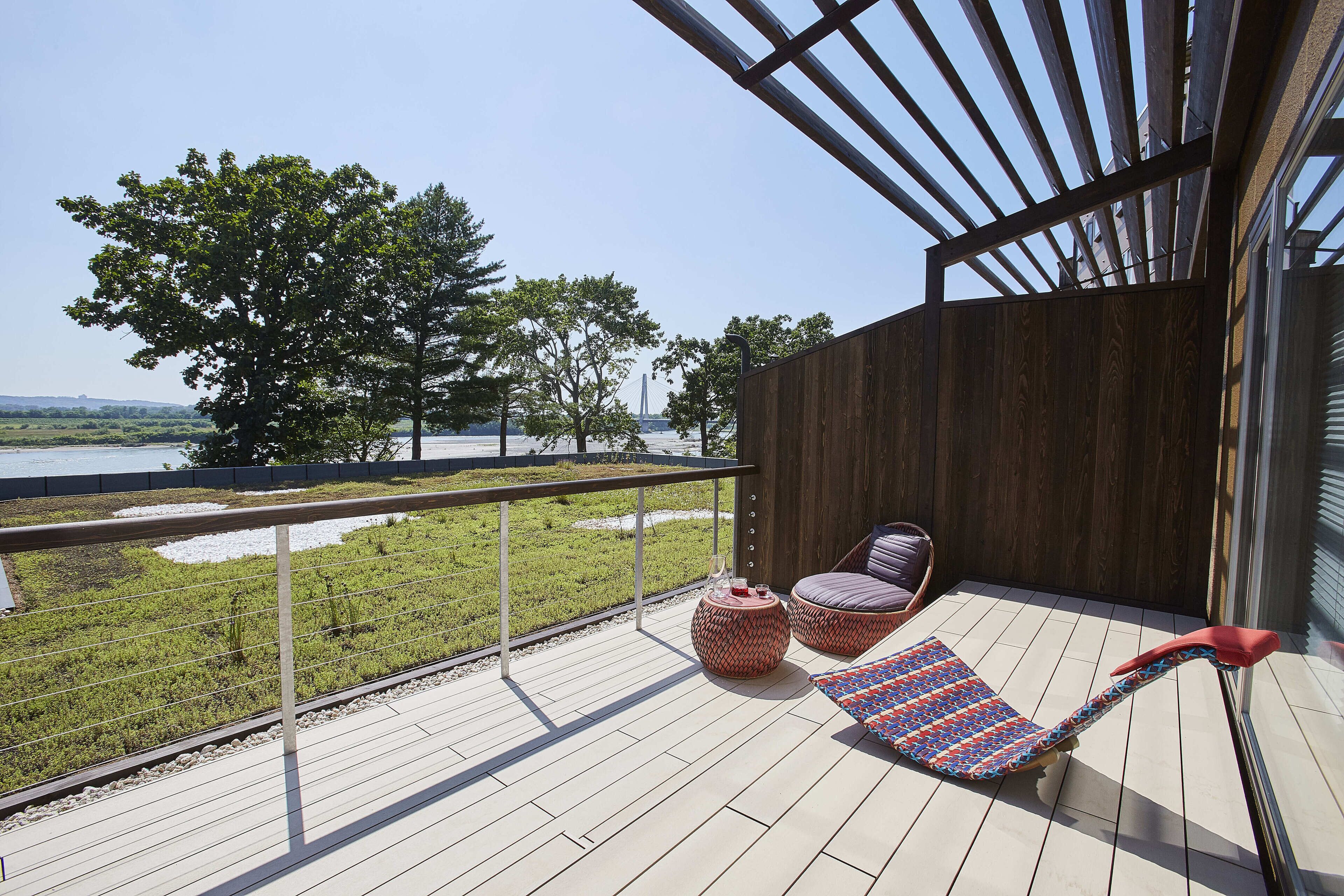 A balcony with a wooden floor, two wicker chairs, a small round table, and a colorful rug.