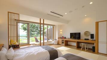 A modern hotel room with two beds, a desk, a TV, and a large window offering a view of the outdoors.