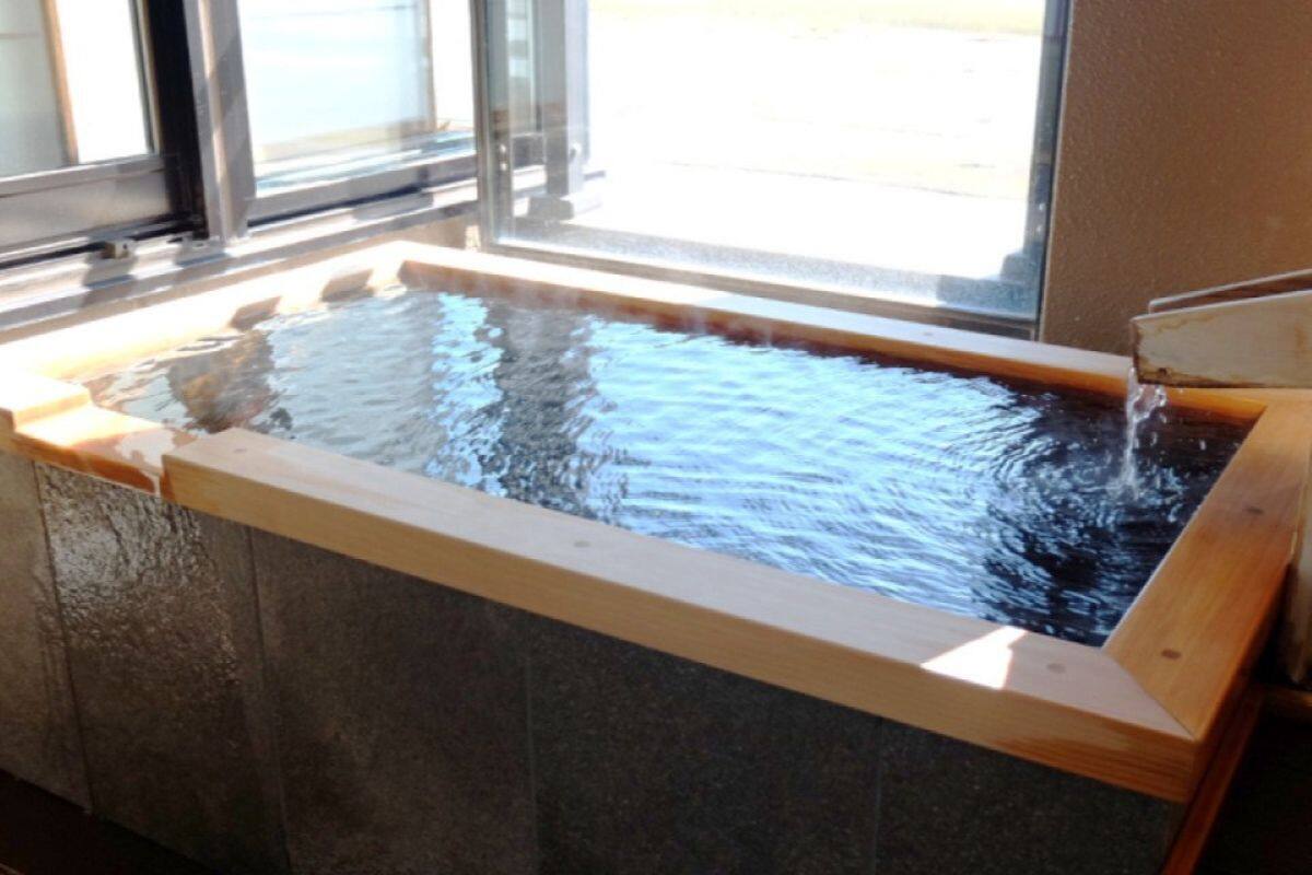 A stone-lined hot tub with a wooden edge, positioned near a window.