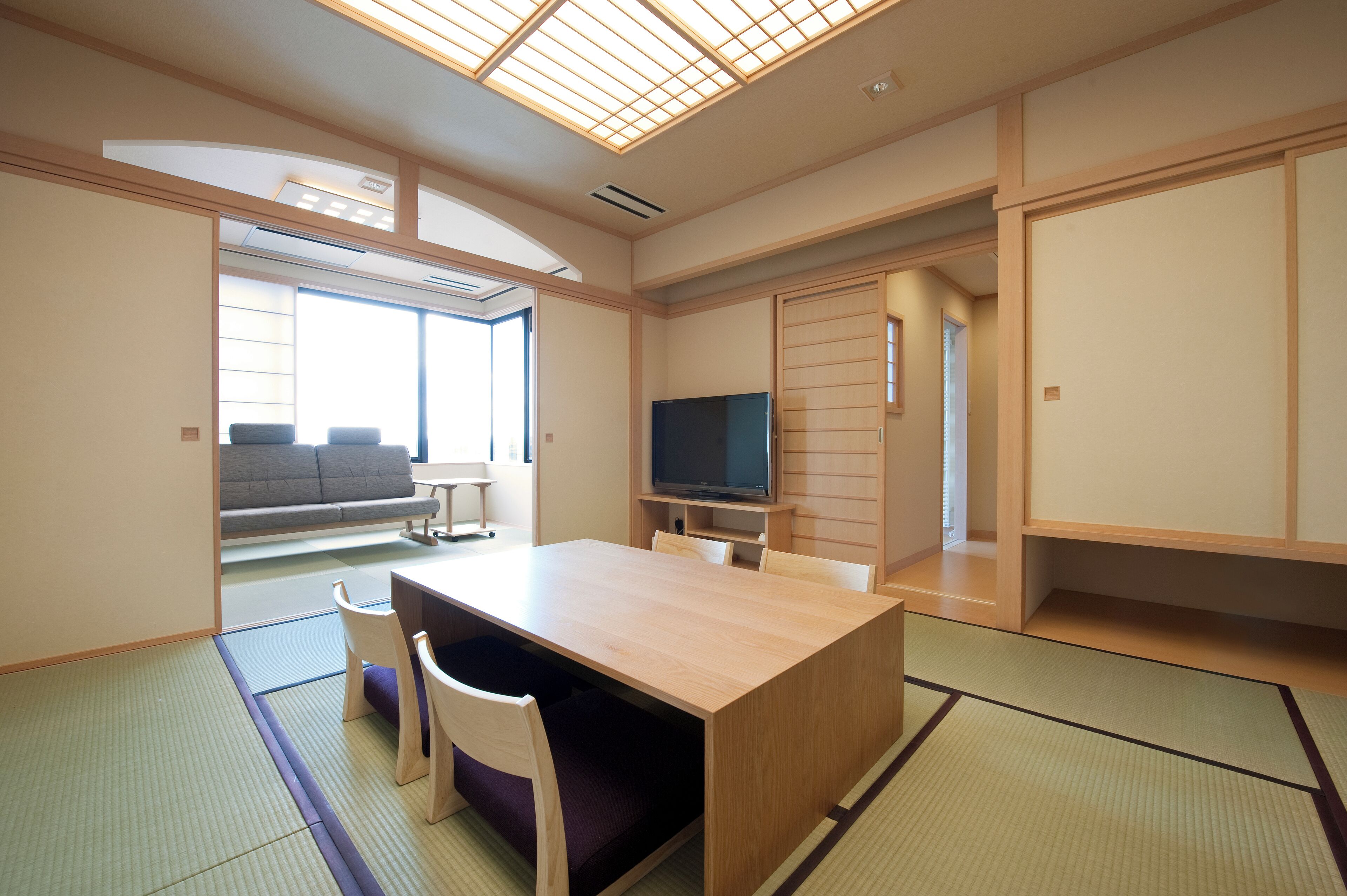 Una habitación de estilo japonés tradicional con suelo de tatami, una mesa baja con sillas, un televisor y puertas correderas.