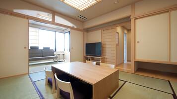 Una habitación de estilo japonés tradicional con suelo de tatami, una mesa baja con sillas, un televisor y puertas correderas.