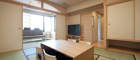 Una habitación de estilo japonés tradicional con suelo de tatami, una mesa baja con sillas, un televisor y puertas correderas.