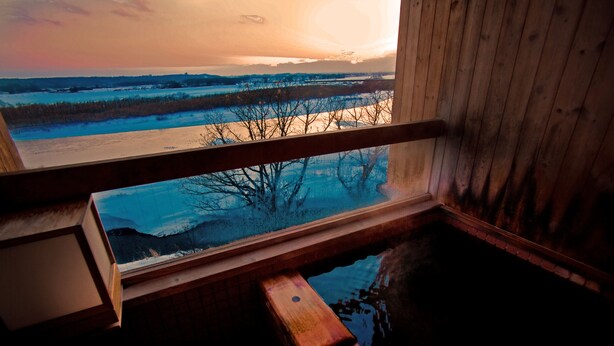 A wooden cabin with a window overlooking a frozen landscape during sunset. - Kangetsuen (Otofuke)