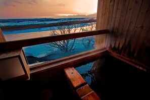 A wooden cabin with a window overlooking a frozen landscape during sunset. - Kangetsuen (Otofuke)