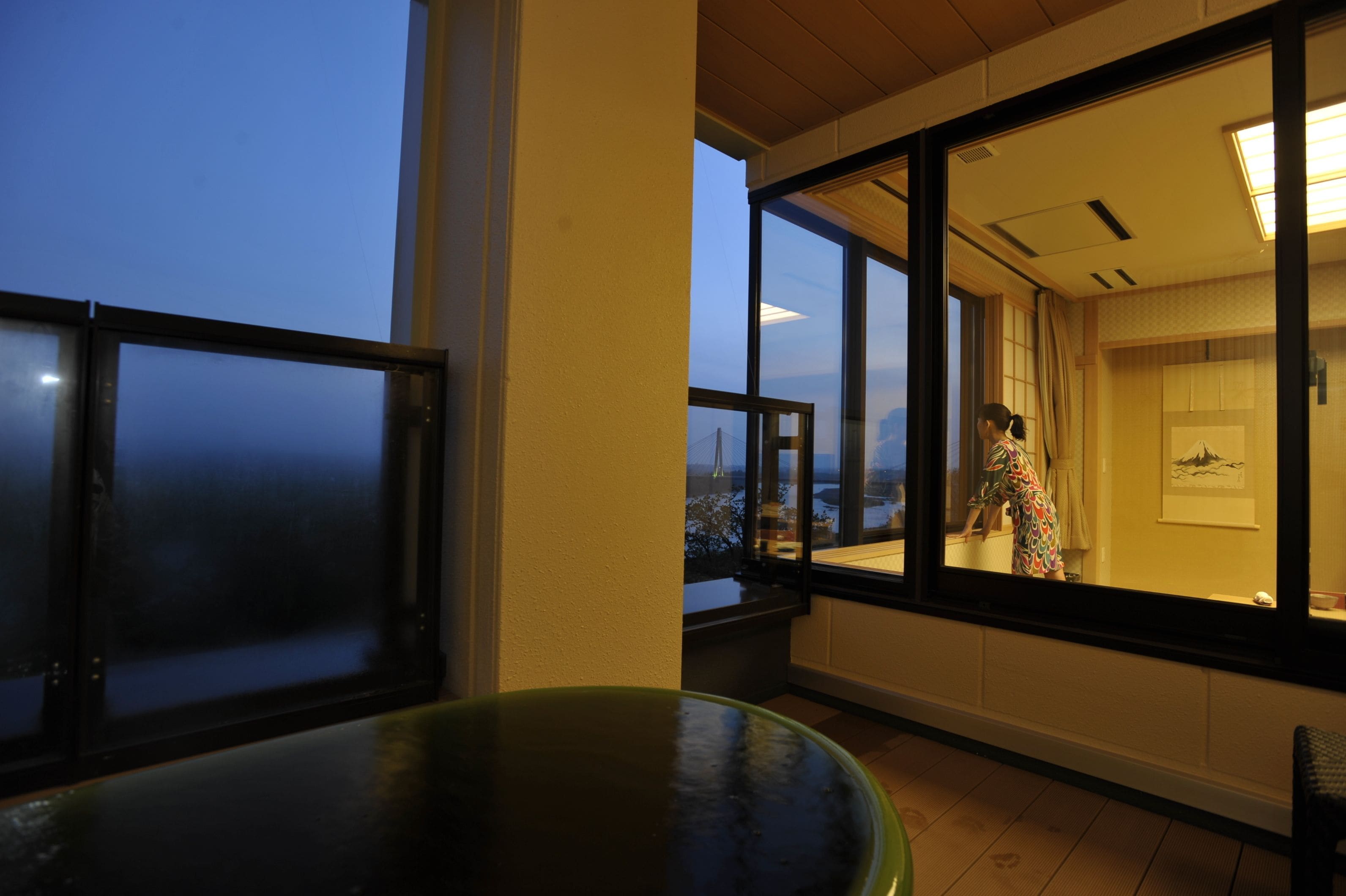 Una habitación con ventanas amplias, vista a un puente y una persona con un vestido estampado.