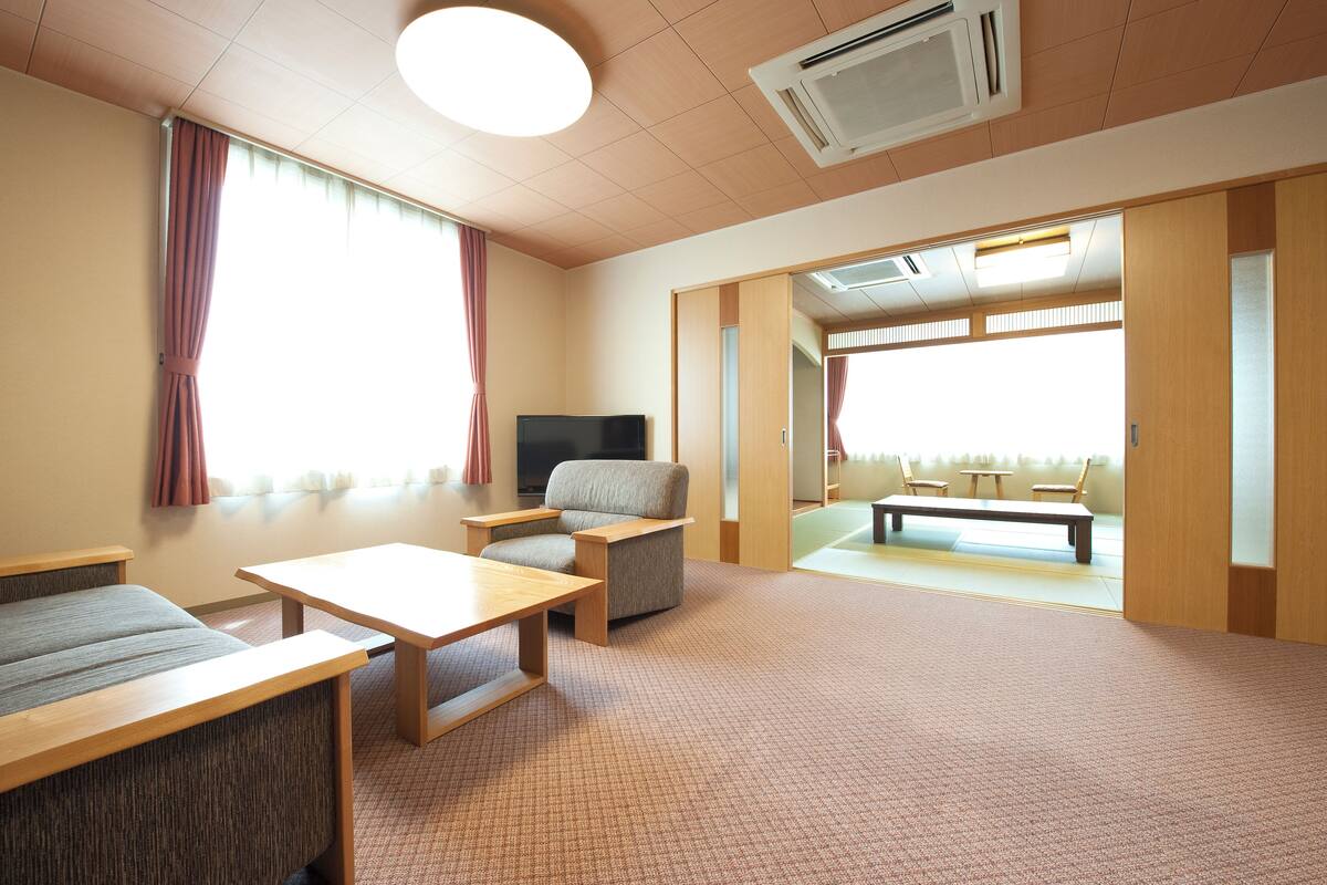 A hotel room with a sofa, a chair, a small table, a television, and a sliding door leading to a balcony.