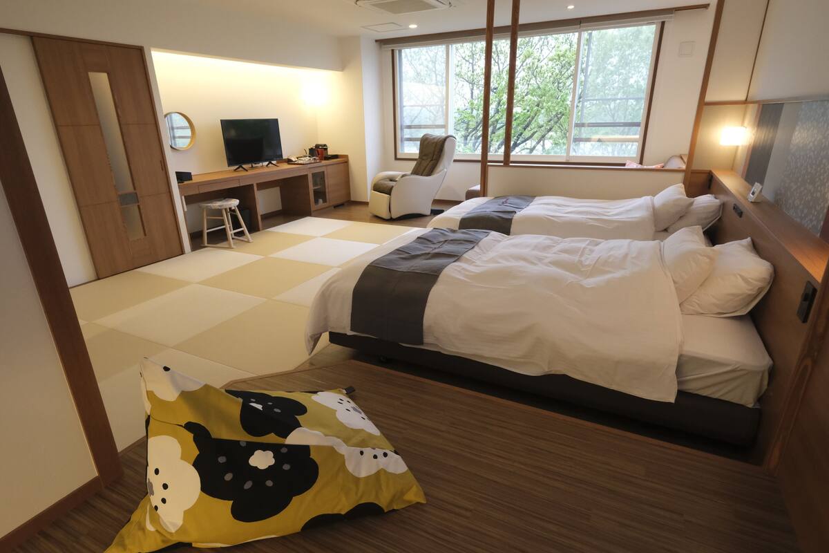 A hotel room with two beds, a desk with a TV, a chair, and a large window.