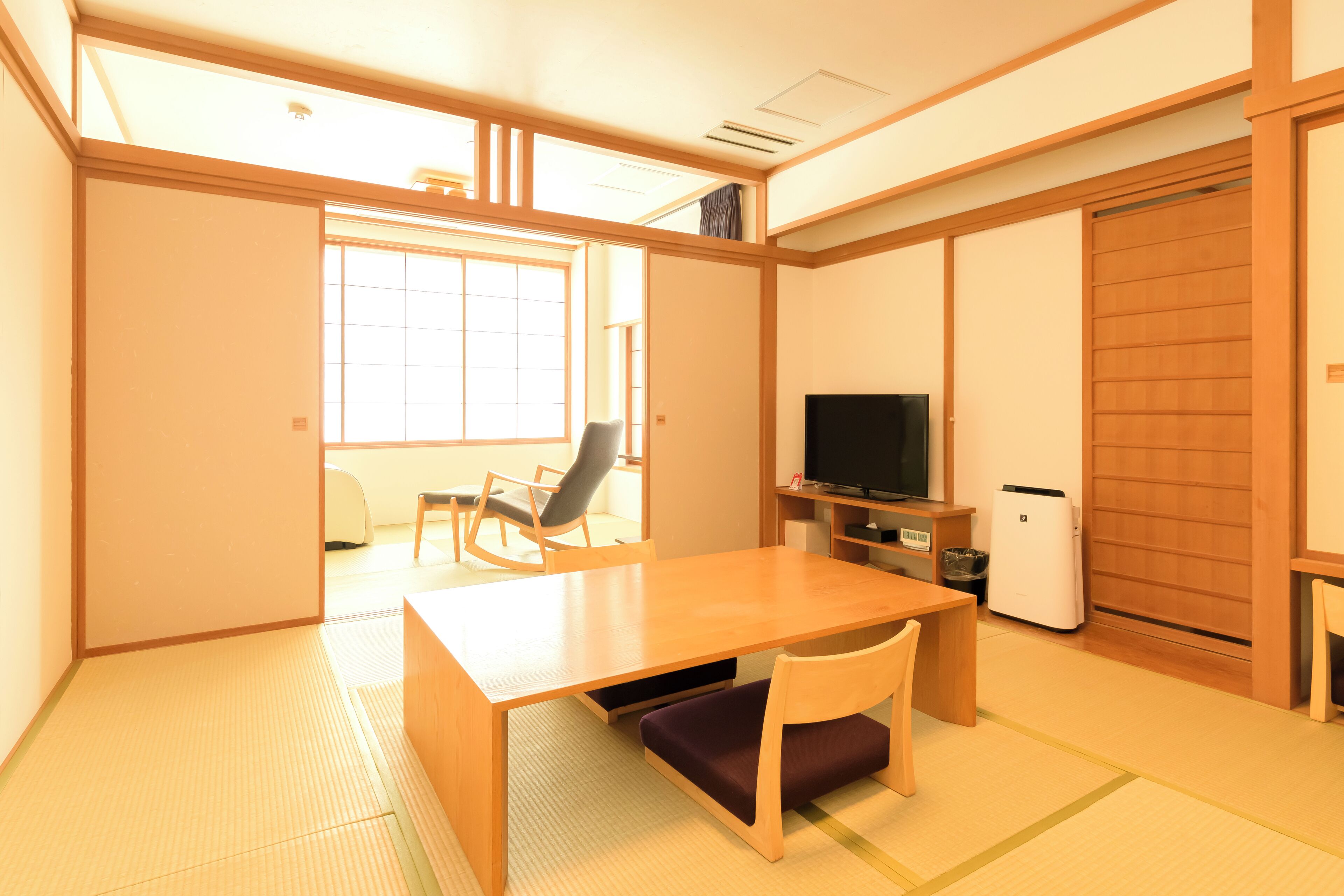 Ein Zimmer mit Tatami-Böden, einem Holztisch, einem Fernseher und einer Schiebetür.