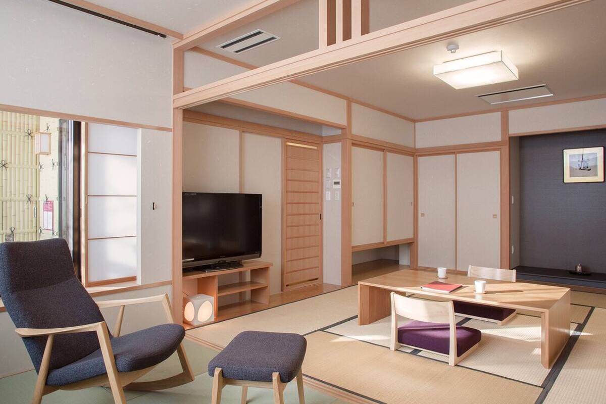 A traditional Japanese-style living room with tatami flooring, a television, and a low wooden table with cushions.