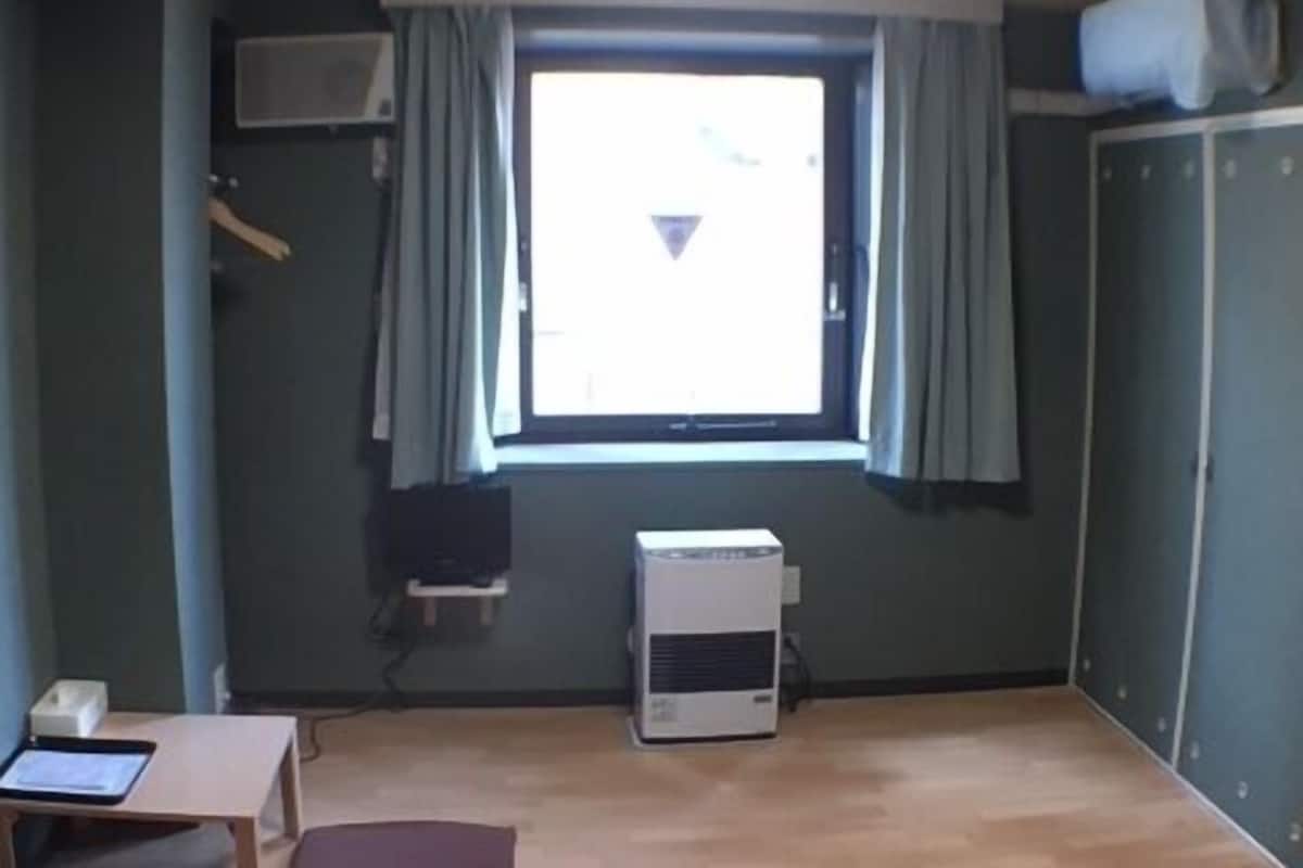 Quarto com uma janela grande, uma pequena mesa com um tablet, um travesseiro vermelho, um ar condicionado branco e um guarda-roupa.