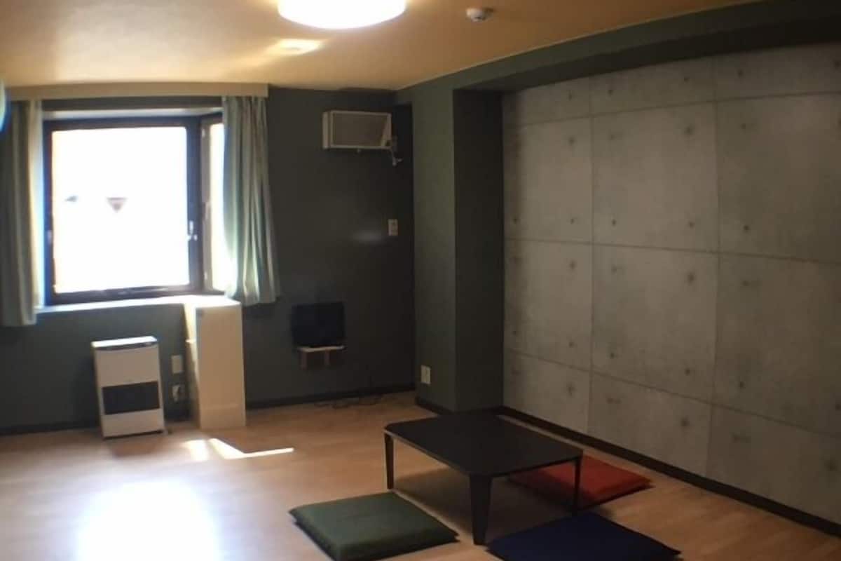 Quarto com uma janela grande, uma mesa pequena, um banco e uma área de estar acolchoada.