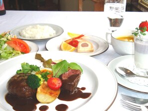 A table set with various dishes including a meat dish with vegetables, a bowl of rice, and a glass of a light-colored beverage. - Pension Ing Tomamu (Shimukappu)